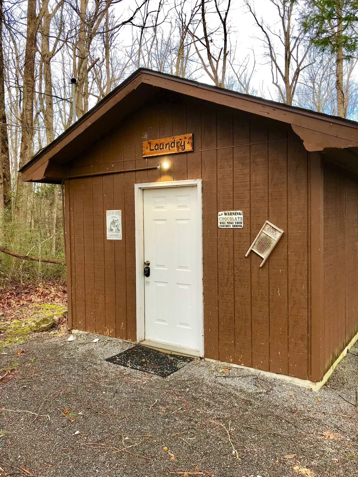 This exterior shot features a welcoming gravel path leading to a white door, accented by a playful 'Laundry' sign. The outdoor setting hints at communal or family activities, with an atmosphere that is both casual and inviting. Natural surroundings and the open entry create a sense of arrival and connection to the outdoors.