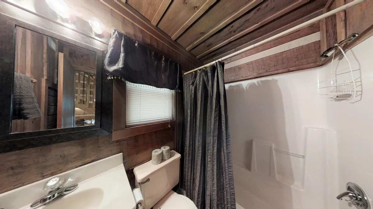 This image reveals a welcoming bathroom interior with a rustic wooden ceiling, a mirror above the sink, a neatly arranged countertop, a toilet, and a shower curtain. The scene exudes a sense of comfort and practicality, ideal for freshening up after a day spent outdoors.