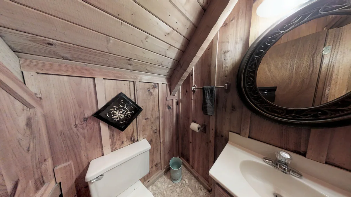 A compact, rustic half bath with wooden walls, a mirror, a sink, a toilet, and decorative art, creating an intimate yet charming ambiance for quick refreshment or private moments.