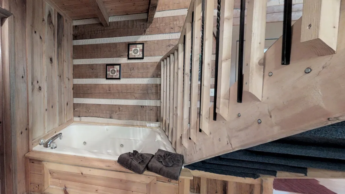 A tranquil, comfortable indoor space featuring a spacious jacuzzi tub, wooden staircase, framed artwork, and neatly arranged towels. The inviting jacuzzi area is adjacent to the living space, highlighting the open layout and the blend of relaxation and social spaces as described in the section content.